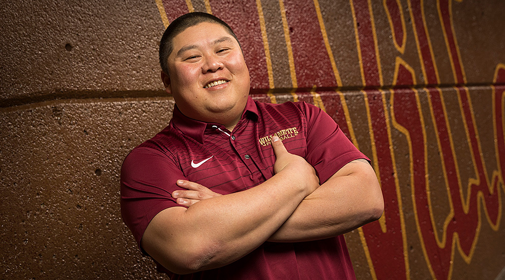 Isaac Parker, smiling while standing against a wall painted with Willamette's word logo. 